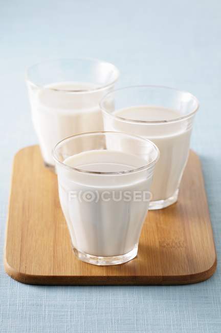 Vasos de leche sobre tabla de cortar madera - foto de stock