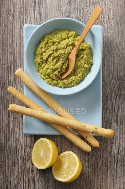 Guacamole, grissini and lemons in blue bowl over woden surface — Stock Photo