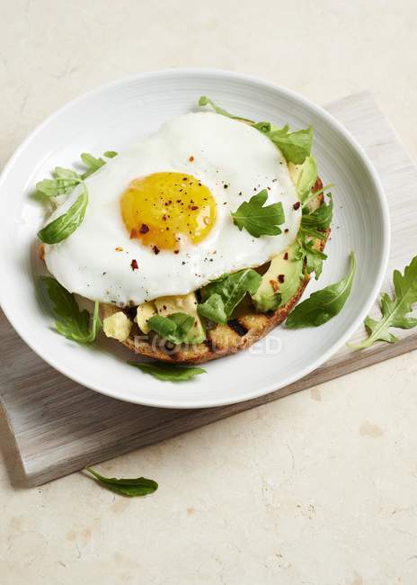 A fried egg and avocado on toast  on white plate over woden desk — Stock Photo