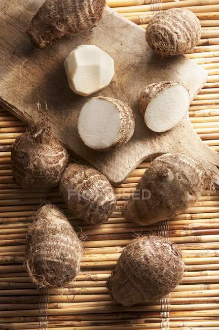 Taro roots, whole and halved on chopping desk — Stock Photo