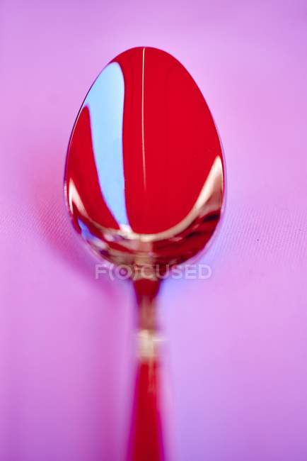 Vista close-up de uma colher vermelha em uma superfície rosa — Fotografia de Stock