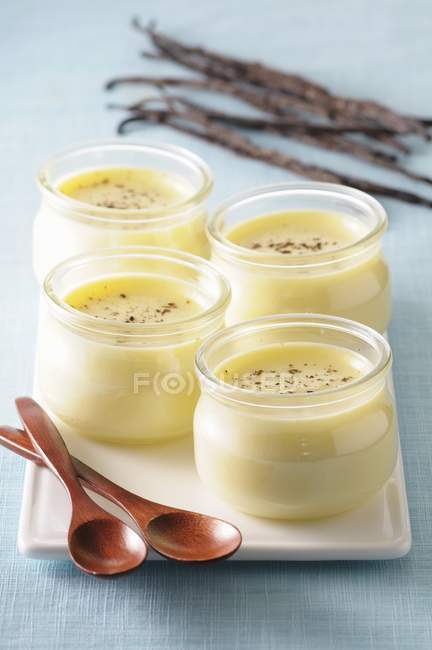 Vue rapprochée de quatre verres de crème vanille avec cuillères en bois sur plateau — Photo de stock