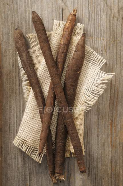 Negro salsify en un paño beige sobre la superficie de madera - foto de stock