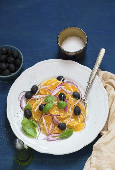Orangensalat mit Oliven, Zwiebeln und Basilikum auf weißem Teller mit Gabel — Stockfoto