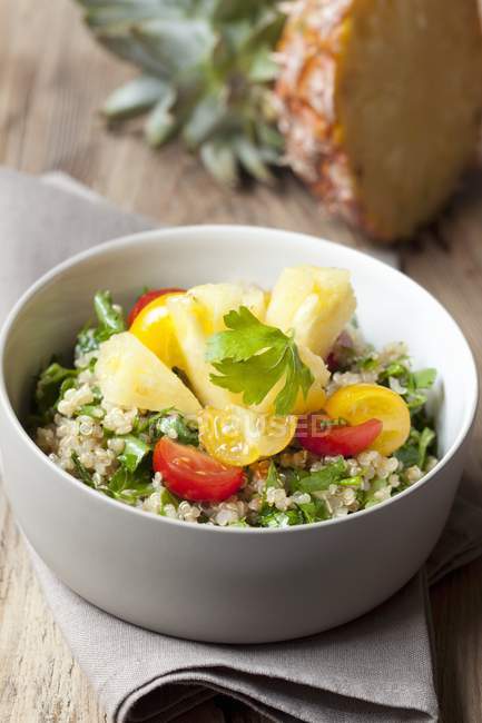 Quinoa salad with tomatoes and pineapple in white bowl over towel — Stock Photo