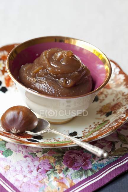 Closeup view of chestnut cream in bowl with spoon and chestnut on saucer — Stock Photo