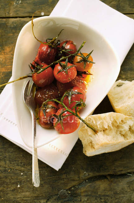 Tomates cereja fritos marinados; pão branco em prato branco sobre toalha — Fotografia de Stock