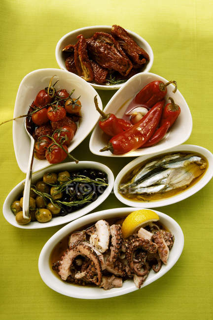 Surtido de antipasti: verduras en vinagre, pescado, pulpo en la superficie verde - foto de stock