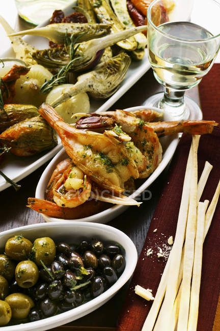 Antipasti platter, scampi and olives; grissini on red cloth — Stock Photo