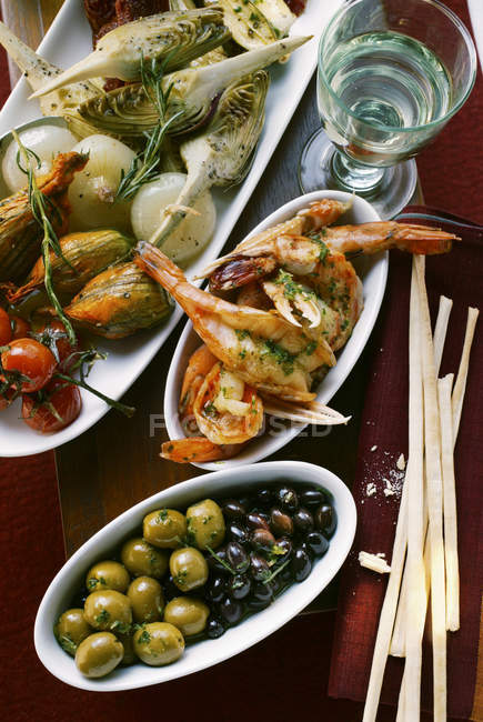 Antipasti platter, scampi and olives; grissini in white dishes — Stock Photo