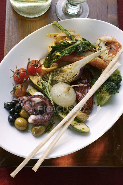 Antipasti platter with wooden sticks of marinated vegetables and seafood — Stock Photo
