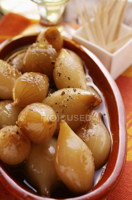 Pickled shallots in brown bowl over red cloth — Stock Photo