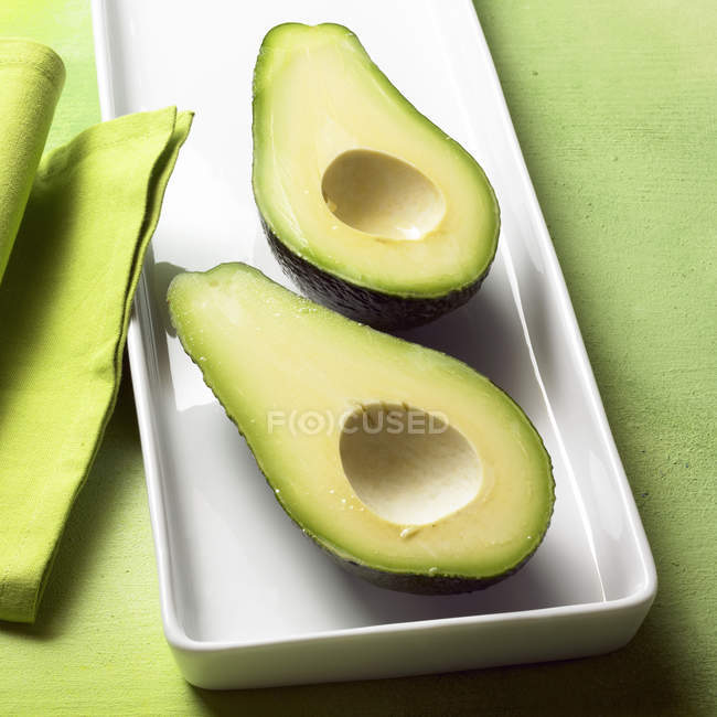 Avocado halves on white platter — Stock Photo