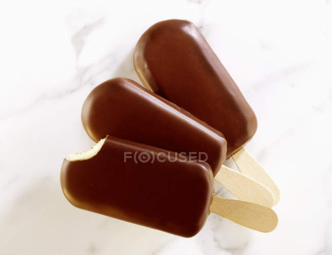 Vista de primer plano de helado de vainilla recubierto de chocolate en palos - foto de stock