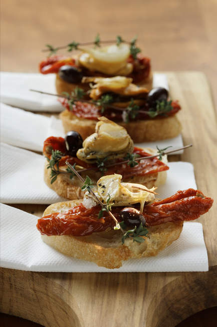 Crostini with seafood and dried tomatoes on wooden chopping board — Stock Photo