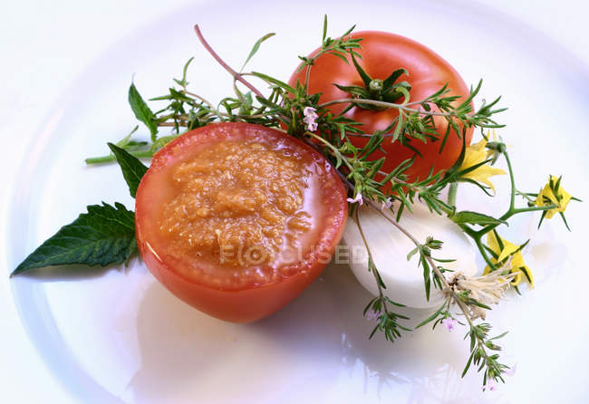 Tomato sauce in hollowed-out tomato; fresh herbs  on white plate — Stock Photo