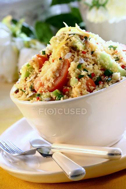 Couscous salad with vegetables in white bowl over plate with fork and knife — Stock Photo