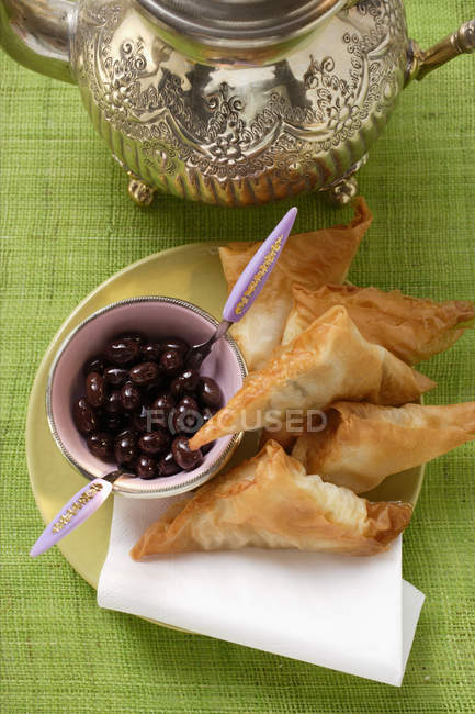 Savoury pasties and black olives over green surface — Stock Photo