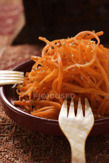 Ensalada de zanahoria cruda con sésamo en plato marrón con tenedores - foto de stock