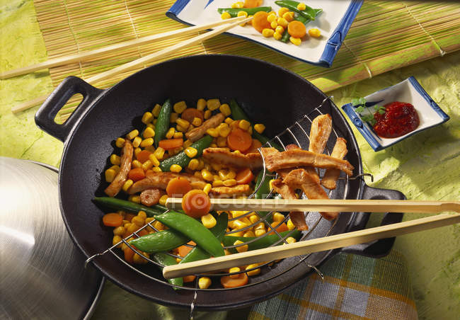 Meat and vegetables in wok with wooden sticks — Stock Photo