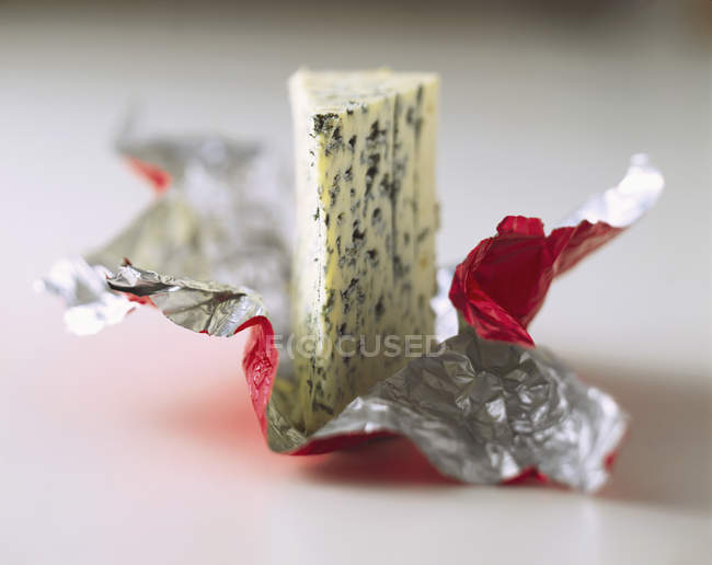 A piece of Roquefort on plastic packaging on white surface — Stock Photo