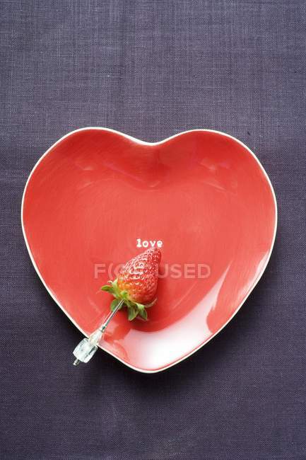 Strawberry on red heart-shaped plate — Stock Photo