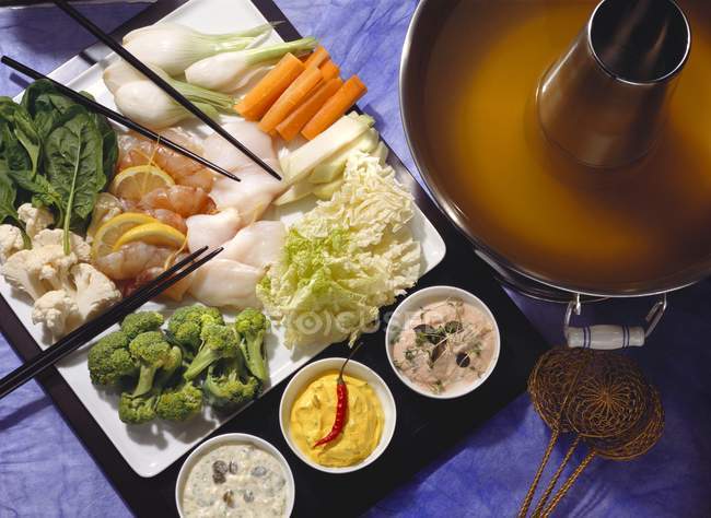 Fondue de verduras con pescado y salsas en la superficie azul - foto de stock
