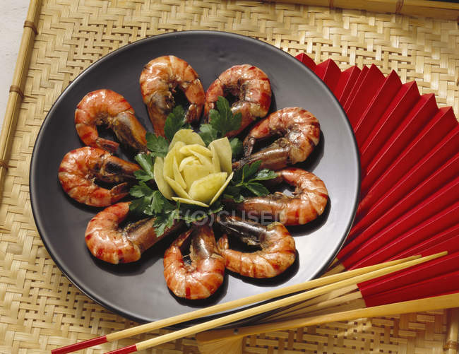 Stewed Norway Lobsters on black plate over straw mat with chopsticks — Stock Photo