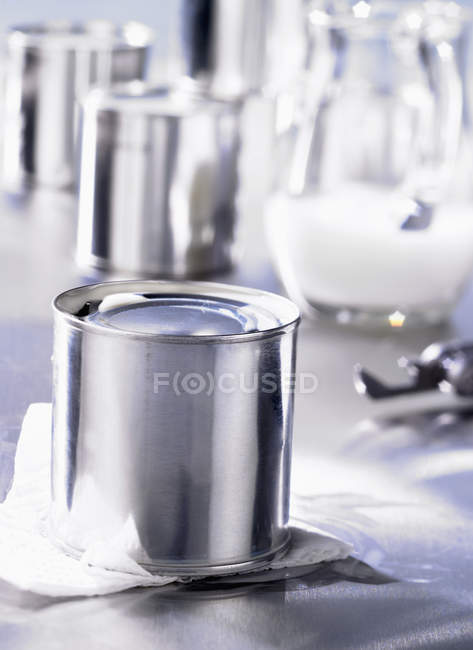 Closeup view of tinned milk with milk pitcher on background — Stock Photo