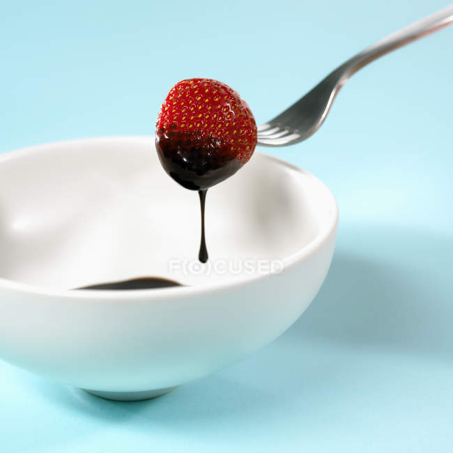 Closeup view of dipped in chocolate strawberry on fork over bowl — Stock Photo