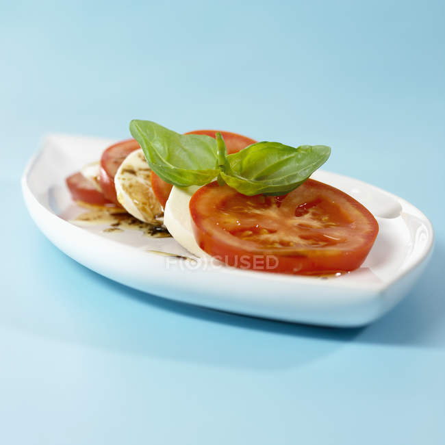 Mozzarella, pomodori e basilico su placca bianca su superficie blu — Foto stock