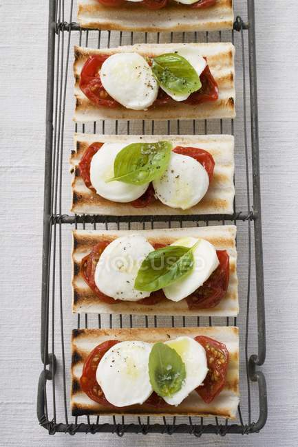 Tomatoes, mozzarella and basil on grilled bread over white surface — Stock Photo