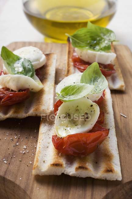 Tomatoes and mozzarella on grilled bread, olive oil behind over wooden desk — Stock Photo