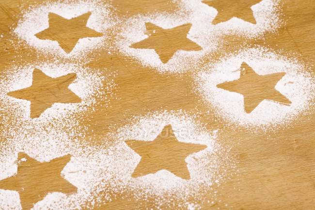 Closeup view of star shapes outlined in icing sugar on wooden background — Stock Photo