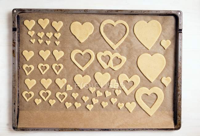 Top view of heart-shaped cut-out biscuits on baking tray — Stock Photo