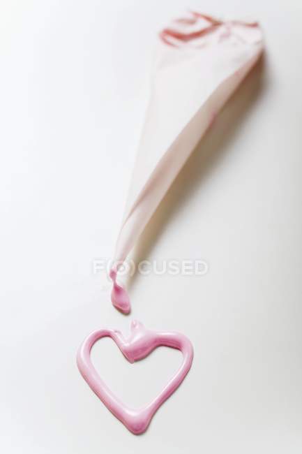 Closeup view of pink heart in glace icing and a piping bag — Stock Photo