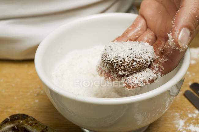 Closeup cropped view of hand coating a biscuit in grated coconut — Stock Photo