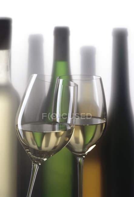 Verres de vin blanc devant les bouteilles — Photo de stock