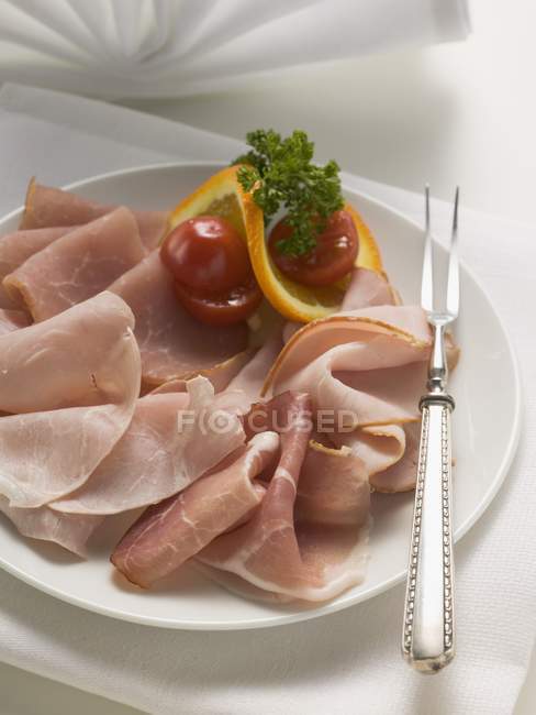 Sliced ham on plate with meat fork — Stock Photo
