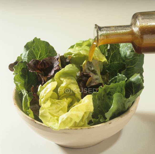 Pouring dressing over mixed lettuce — Stock Photo