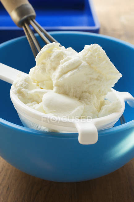 Quark in sieve in blue mixing bowl with whisk — Stock Photo