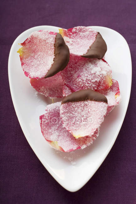 Vista de primer plano de pétalos de rosa bañados en chocolate y azucarados en el plato - foto de stock