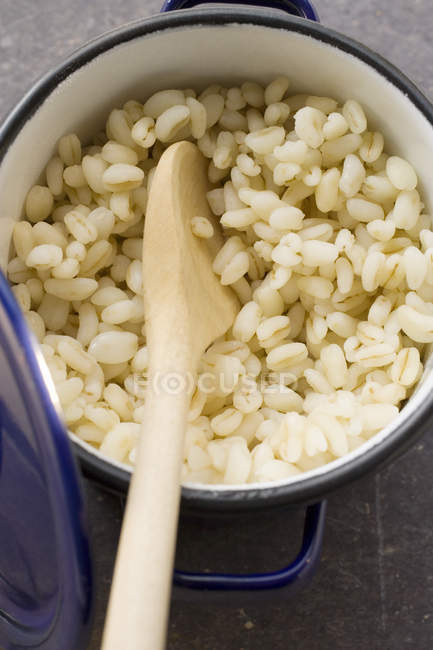 Closeup view of cooked barley in bowl with wooden spoon — Stock Photo