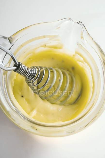 Primer plano vista superior de la salsa holandesa con un batidor en una pequeña sartén de vidrio - foto de stock