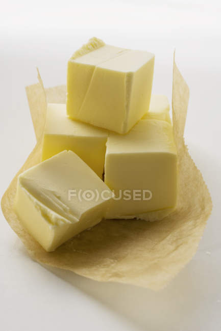 Vista de cerca de los cubos de mantequilla sobre papel - foto de stock