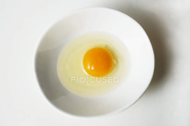 Egg broken into white bowl — Stock Photo