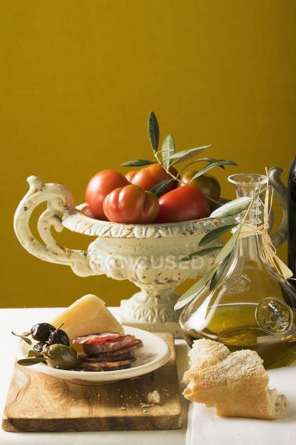 Натюрморт з оливками, нарізаною ковбасою, пармезаном, хлібом, олією та помідорами — стокове фото