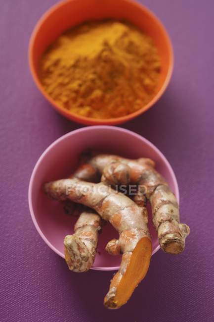 Roots and ground turmeric in bowls — Stock Photo