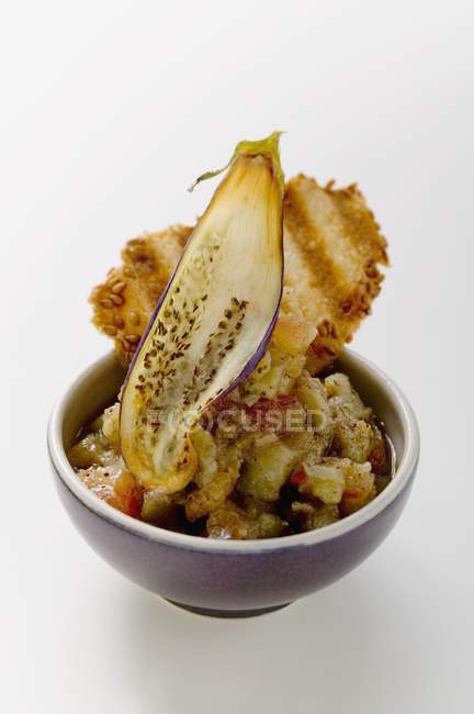 Aubergine salad with sesame cracker in bowl on white background — Stock Photo