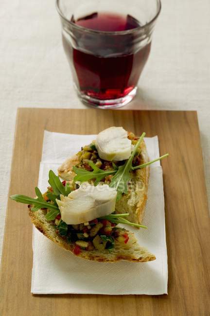 Bruschetta with fish and aubergine paste, red wine on wooden desk with paper — Stock Photo